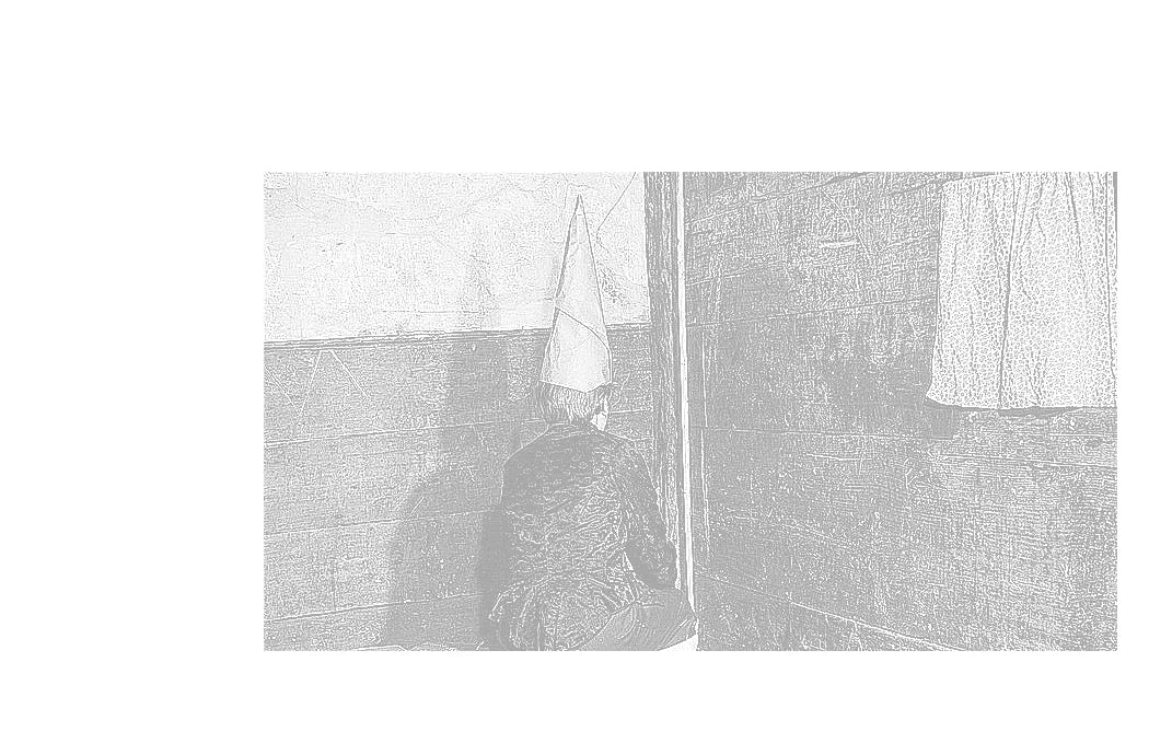 A child in a dunce cap sits facing the corner of a room